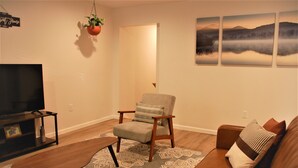 Una sala de estar con televisor de pantalla plana, un sillón gris, un sofá marrón y un tapete estampado.