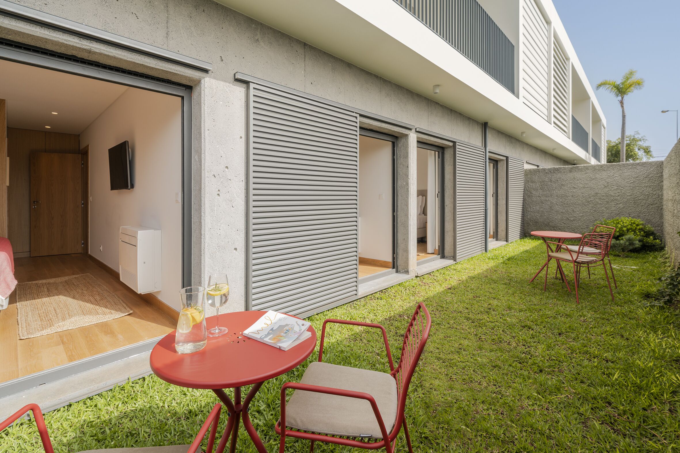 A modern outdoor patio with a red table and chairs, a glass of drink, and a magazine.
