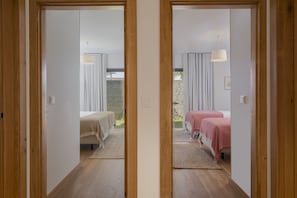 A mirrored view of a room with two beds, a window, and a view of greenery outside.