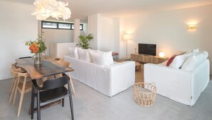 A modern living room with a white sofa, a wooden dining table, and a TV. - Casas do Miradouro 6 by Heart of Funchal (Funchal)