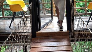 A person entering a room with a view of greenery outside, a wooden deck, and yellow chairs. - Aqeel Cabin in Nature and River (Churuquita Grande)