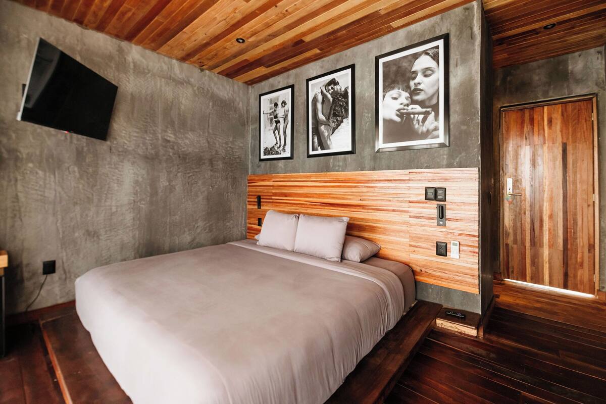 Een slaapkamer met een houten hoofdbord, een bed met een lichtkleurige dekbedovertrek en drie ingelijste foto’s aan de muur.