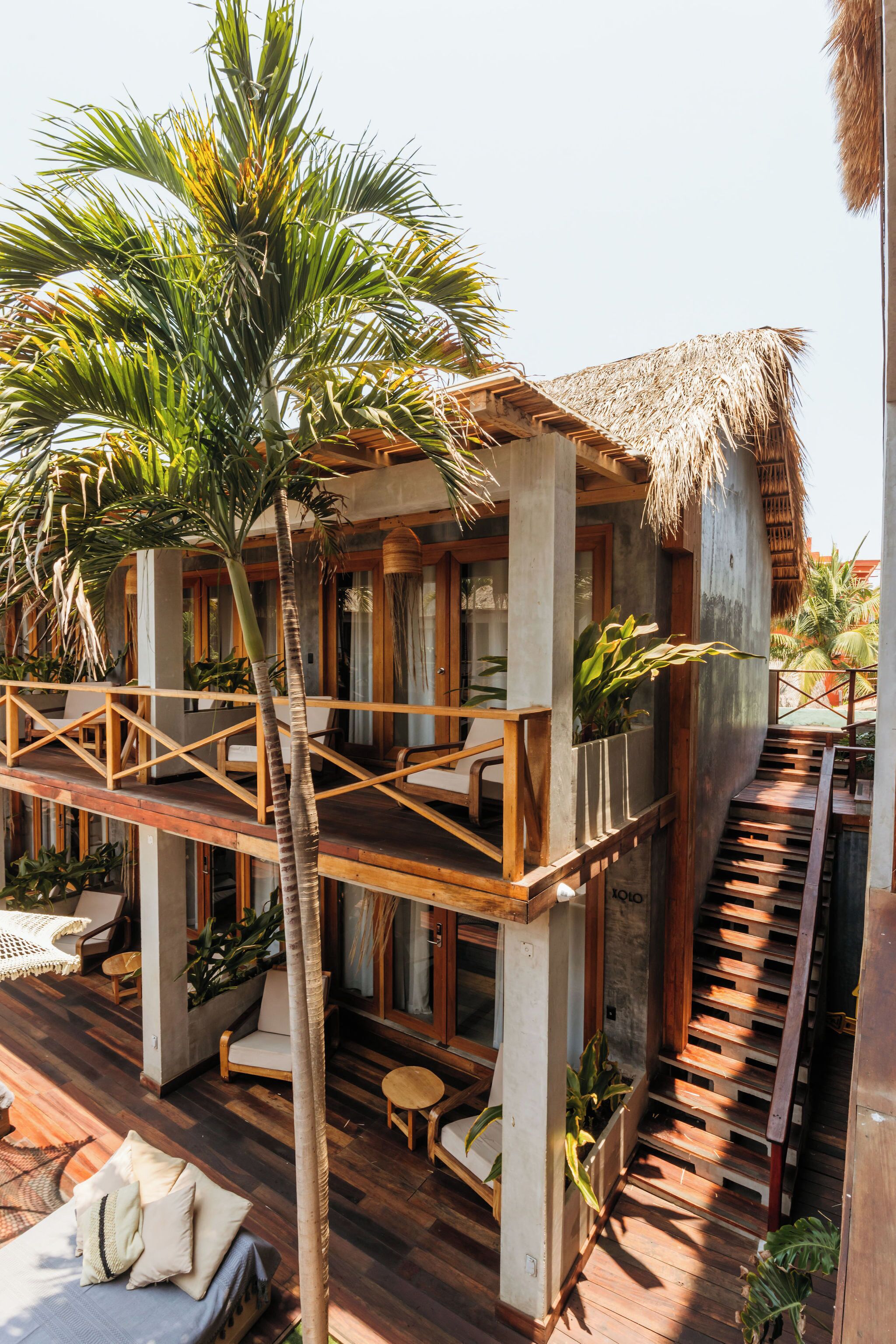 A two-story wooden house with a thatched roof, a balcony, and a staircase.