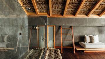 Una habitación moderna con ducha de vidrio, vigas de madera, sofá y alfombra tejida.