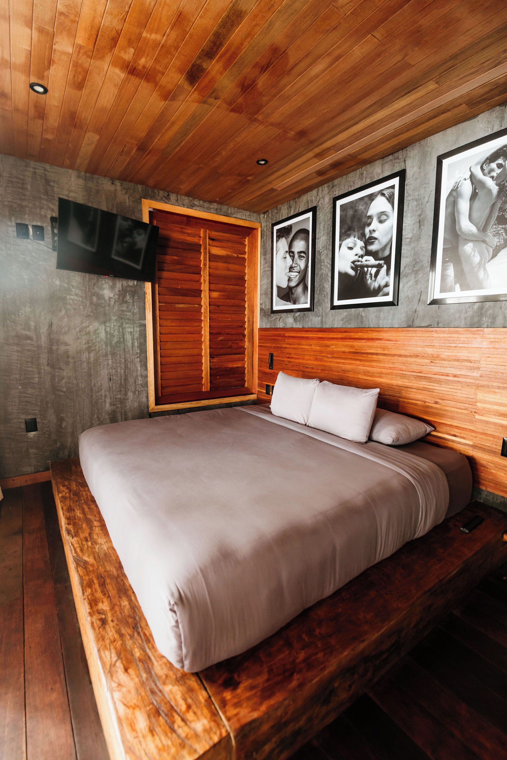 A bedroom with a wooden headboard, a large bed, a wooden bench at the foot of the bed, and a television mounted on the wall.