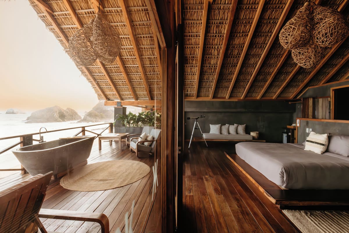 Een houten terras met een ruime badkuip, een bank en een bed met uitzicht op de oceaan.