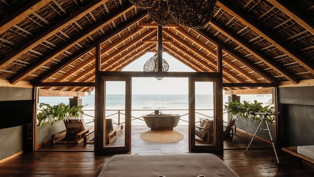 Une pièce spacieuse avec un grand lit, un plancher en bois et une vue sur l’océan par de grandes portes vitrées.