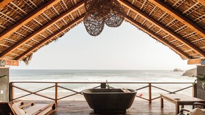 Une terrasse en bois avec une grande baignoire, des chaises longues et une vue sur l’océan.