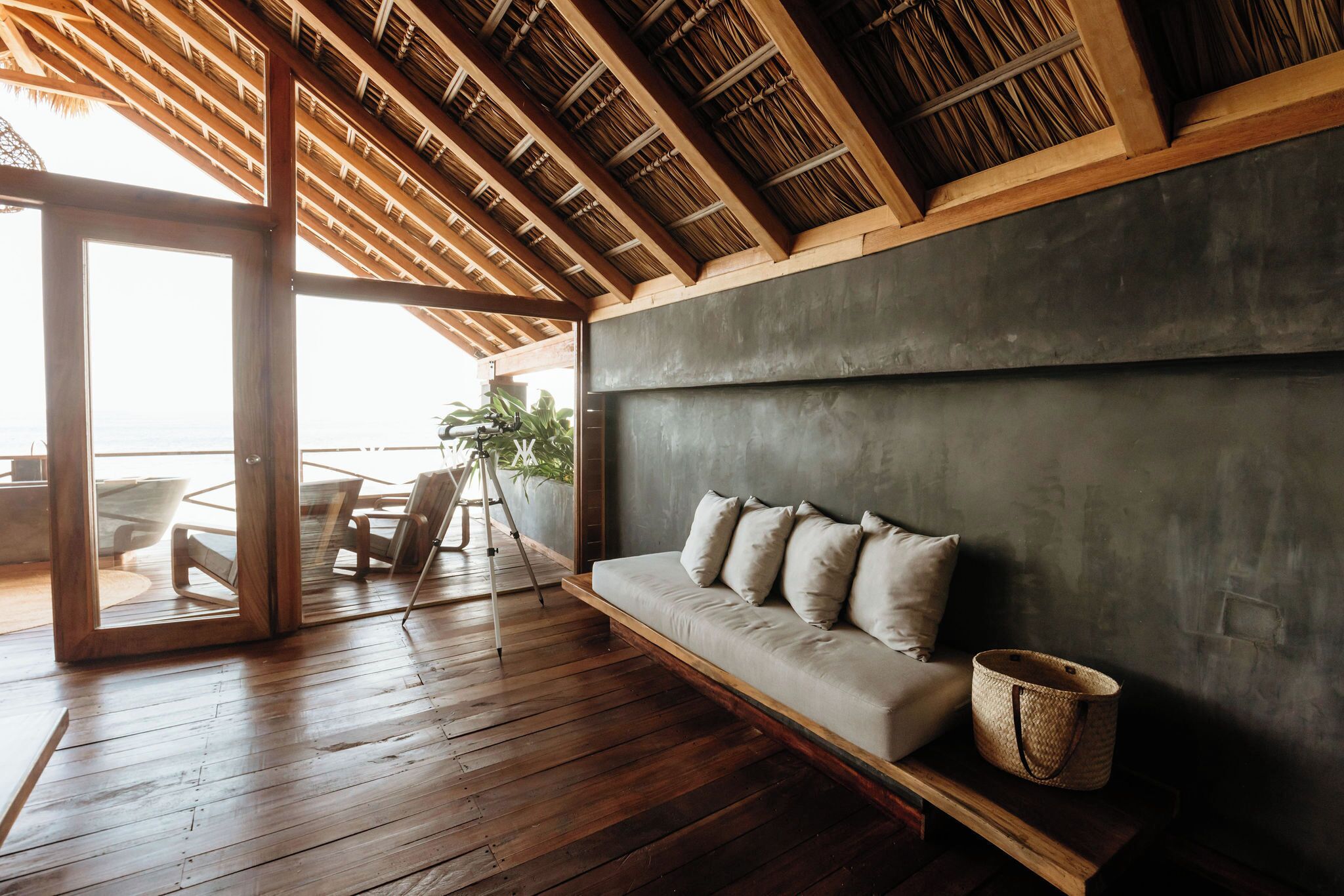 A modern interior with a wooden floor, a sofa with cushions, a tripod, and a large window.
