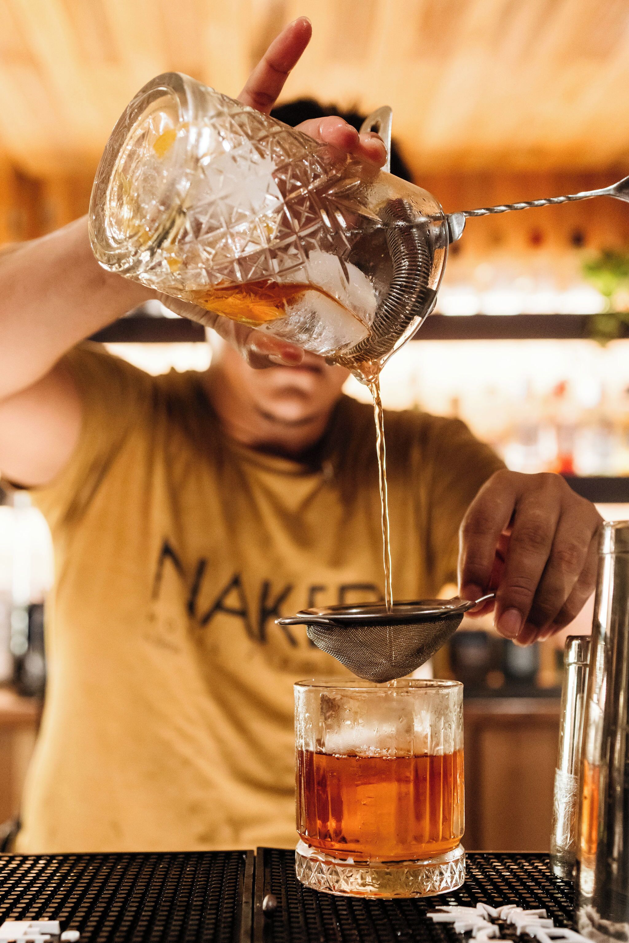 A person pouring a drink from a glass pitcher into a glass through a strainer.