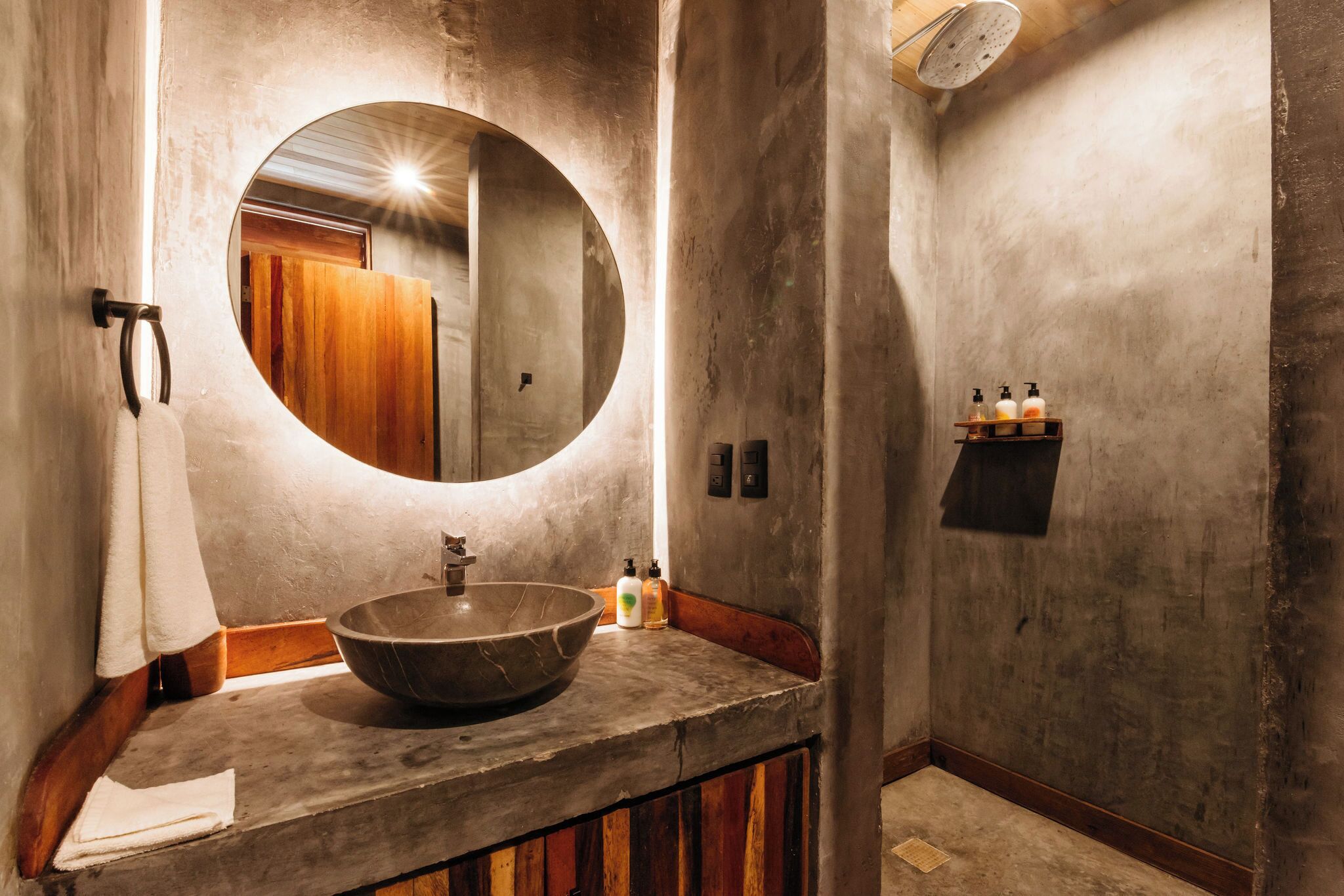 A bathroom with a large round mirror, a vessel sink, wooden paneling, and a towel rack.