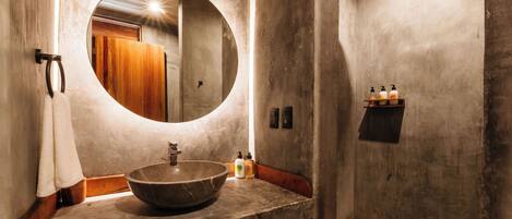 A bathroom with a large round mirror, a vessel sink, wooden paneling, and a towel rack.