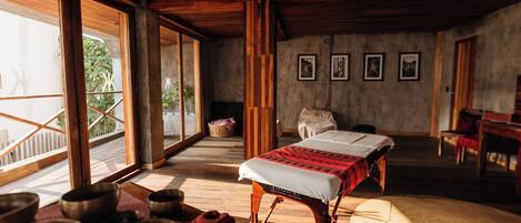 Una habitación con techo de madera, una camilla de masaje y varios cuencos de meditación.
