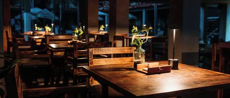 A dimly lit restaurant with wooden tables and chairs, some with potted plants.
