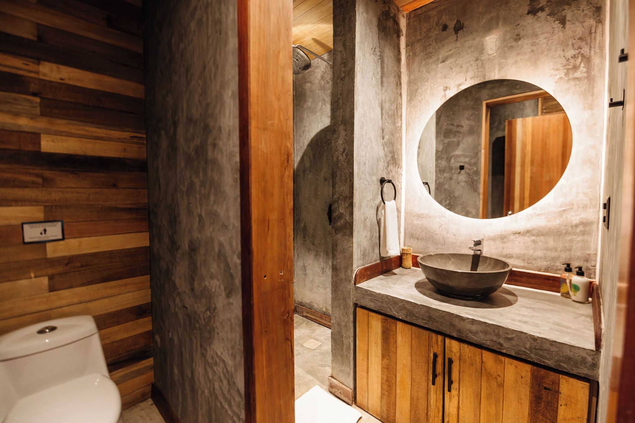 A bathroom with a wooden vanity, a round mirror, and a vessel sink.
