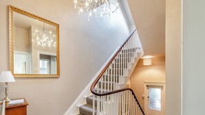 A staircase with white railings and carpeted steps, a large mirror with a gold frame, and a chandelier. - 3 bedroom accommodation in Tenby (Tenby)