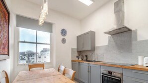 A modern kitchen with grey cabinets, a wooden dining table, and a large window offering a city view. - 3 bedroom accommodation in Tenby (Tenby)