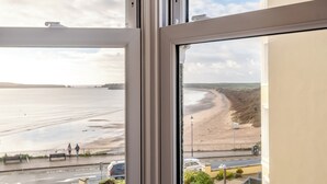 A view from a window overlooking a beach with a road and parked cars in the foreground. - 3 bedroom accommodation in Tenby (Tenby)