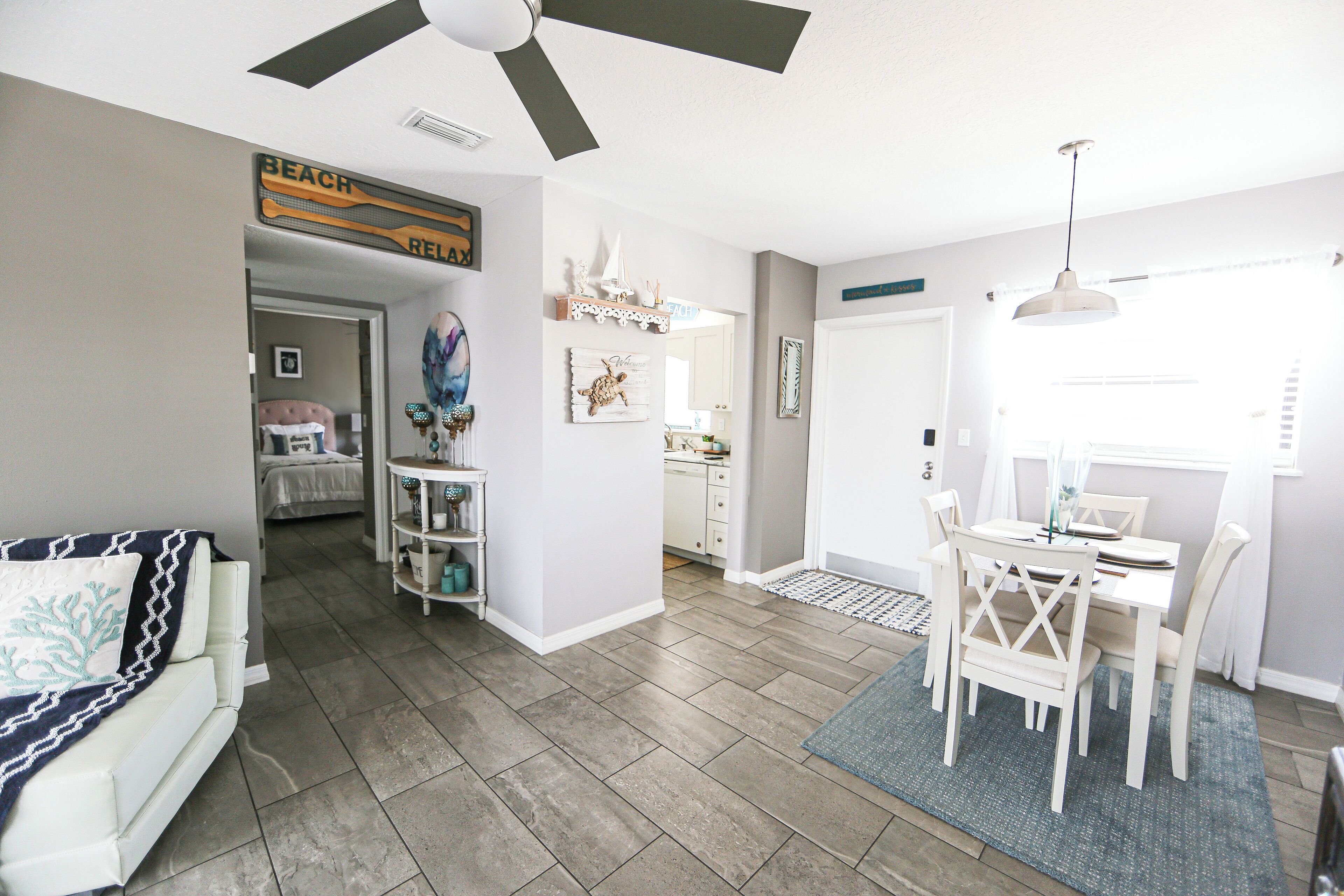 A spacious living area with a ceiling fan, a dining table with chairs, and a kitchen visible through an open doorway.