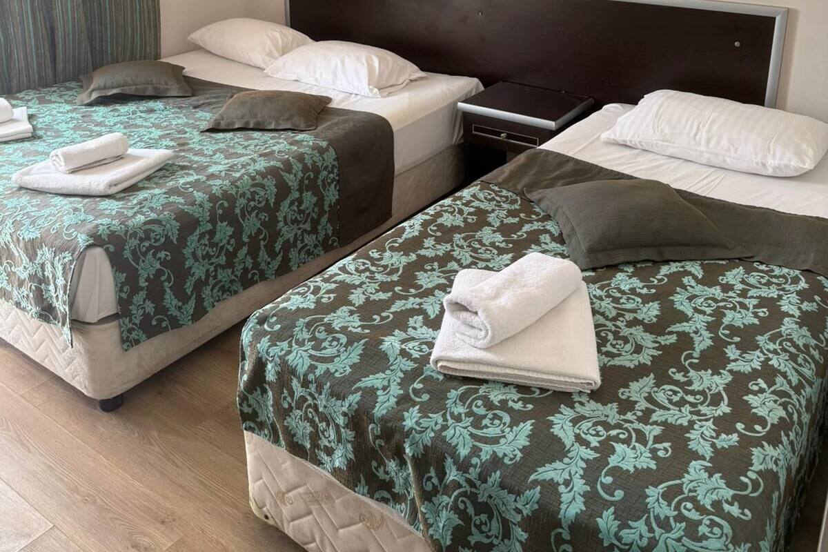 A hotel room with two beds, a nightstand, a wall-mounted light, and a curtain.