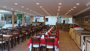 A restaurant with multiple tables and chairs, a kitchen area, and a television screen. - Hotel Gold Stone (Kemer)