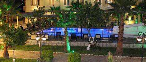 A hotel with a swimming pool, outdoor seating, and palm trees.