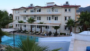A multi-story hotel with a swimming pool, outdoor seating, and palm trees. - Hotel Gold Stone (Kemer)