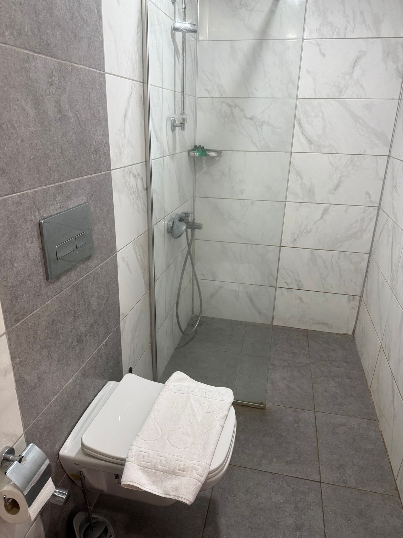 A bathroom with a shower, toilet, and a towel on the seat.