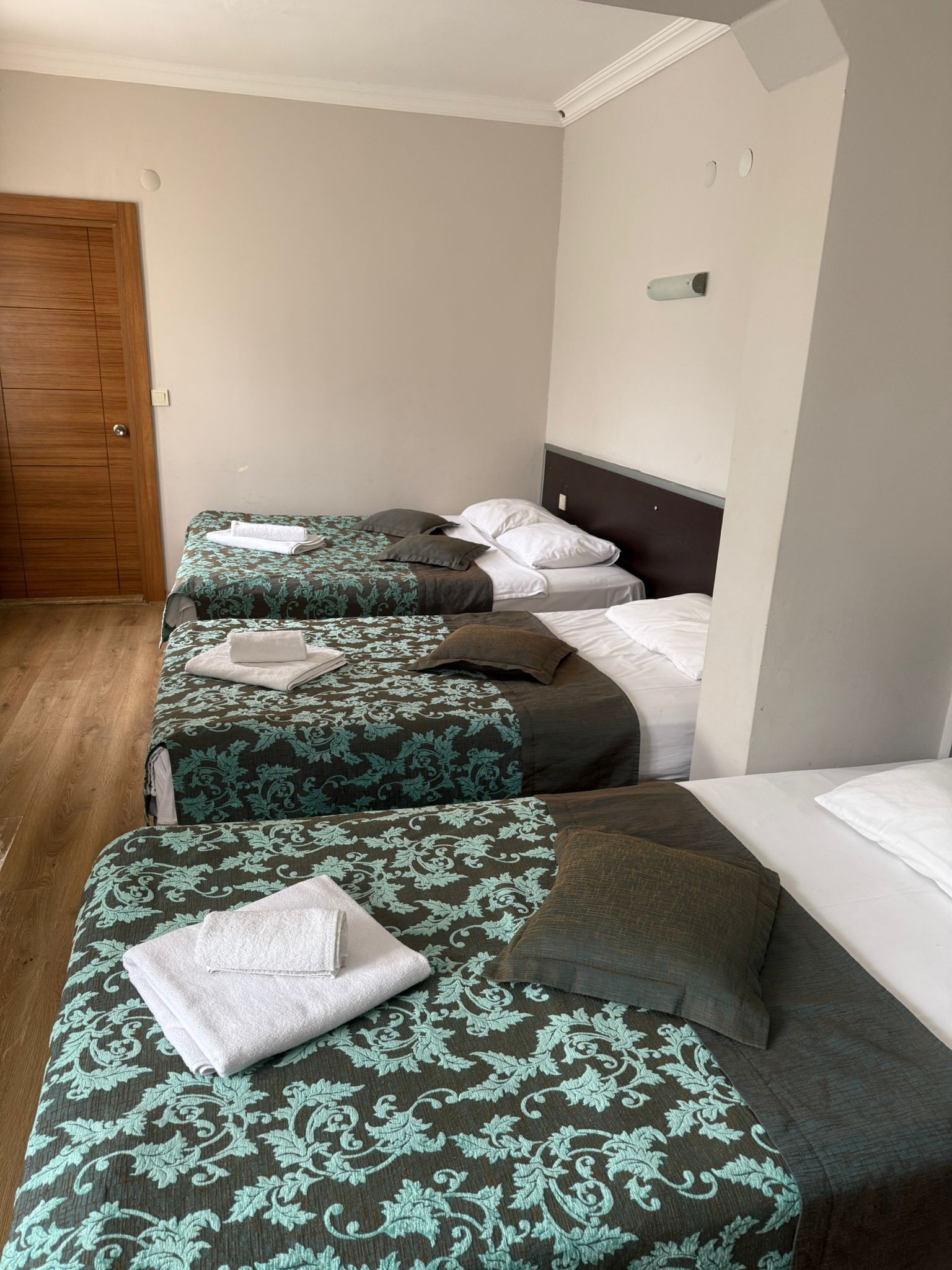 A hotel room with three beds, a wooden wardrobe, and a white ceiling.