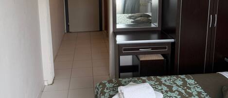 Habitación de hotel con una cama, un escritorio con televisor, un armario y una puerta que da a otra habitación.