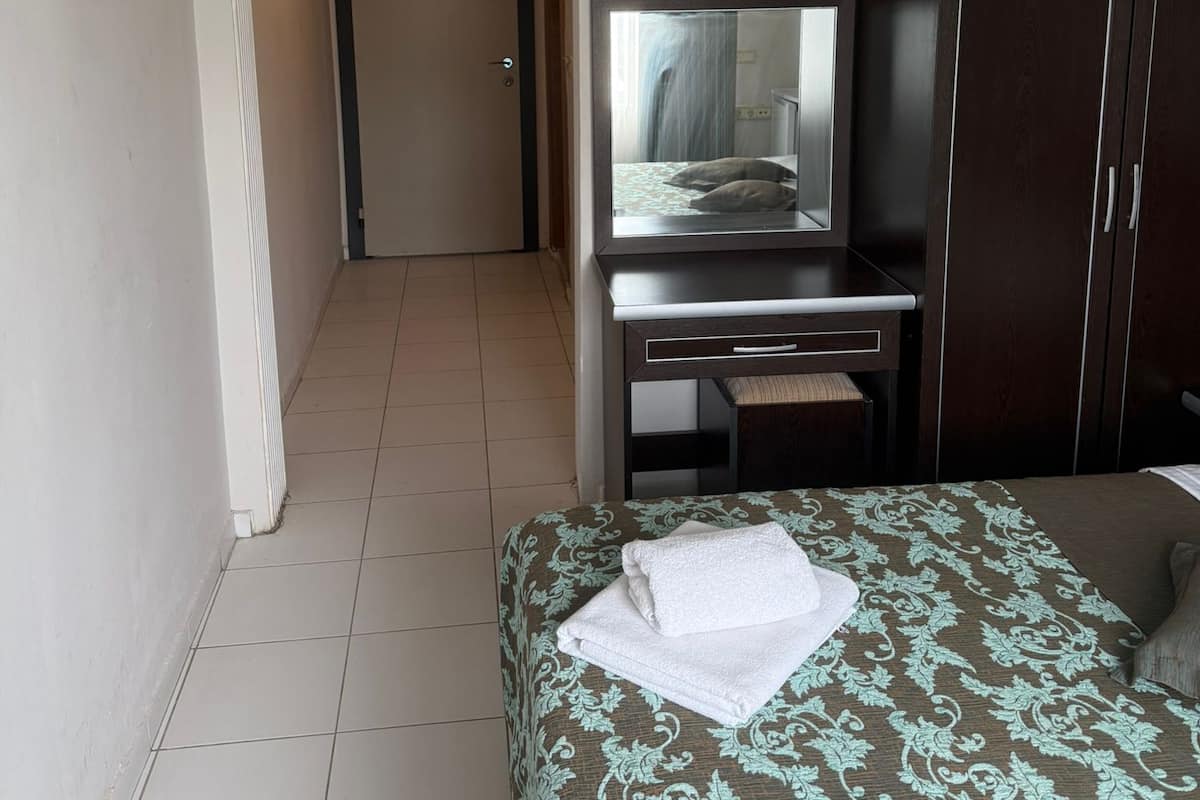 A hotel room with a bed, a desk with a television, a wardrobe, and a door leading to another room.