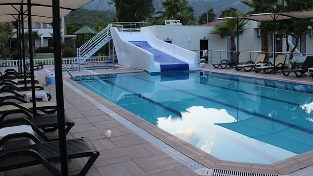 A swimming pool with a slide, lounge chairs, and a mountainous backdrop. - Hotel Gold Stone (Kemer)