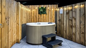 A hot tub with a wooden wall backdrop, a small step leading up to it, and a tiled floor. - We just love this romantic barn conversion. (Skirlaugh)