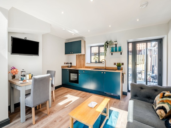Une cuisine moderne avec des armoires bleues, un plan de travail en bois et un four encastré. On y trouve un coin repas avec une table et des chaises, ainsi qu’un canapé agrémenté d’un coussin coloré.