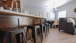 Eine moderne Küche mit einer Holztresen, schwarzen Barhocker und einem Essbereich mit grauem Sofa und einer Pendelleuchte.