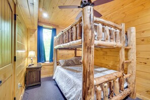 Une chambre dans un chalet en bois, avec un lit superposé, une table de chevet, une lampe et une fenêtre avec des rideaux.
