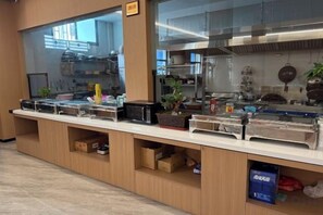 A buffet counter with food containers, a glass display case, and a kitchen area in the background. - Shitai New Century Hotel (Shitai)