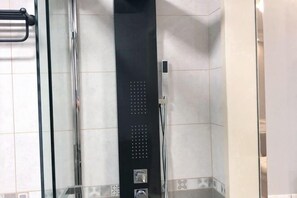 A bathroom with a glass shower enclosure, a black vertical panel with a control panel, and tiled walls with a decorative border. - Shitai New Century Hotel (Shitai)