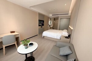 Una habitación de hotel moderna con una cama, un escritorio, una silla, una pequeña mesa con una planta y un sofá con almohadas.