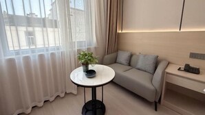 Un salon moderne avec un canapé, une petite table ronde ornée d’une plante et une table de chevet avec un téléphone.