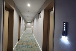 A hotel hallway with a carpeted floor, doors on both sides, and a digital number display on the wall. - Shitai New Century Hotel (Shitai)
