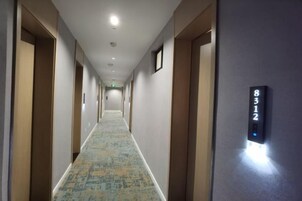 A hotel hallway with a carpeted floor, doors on both sides, and a digital number display on the wall.