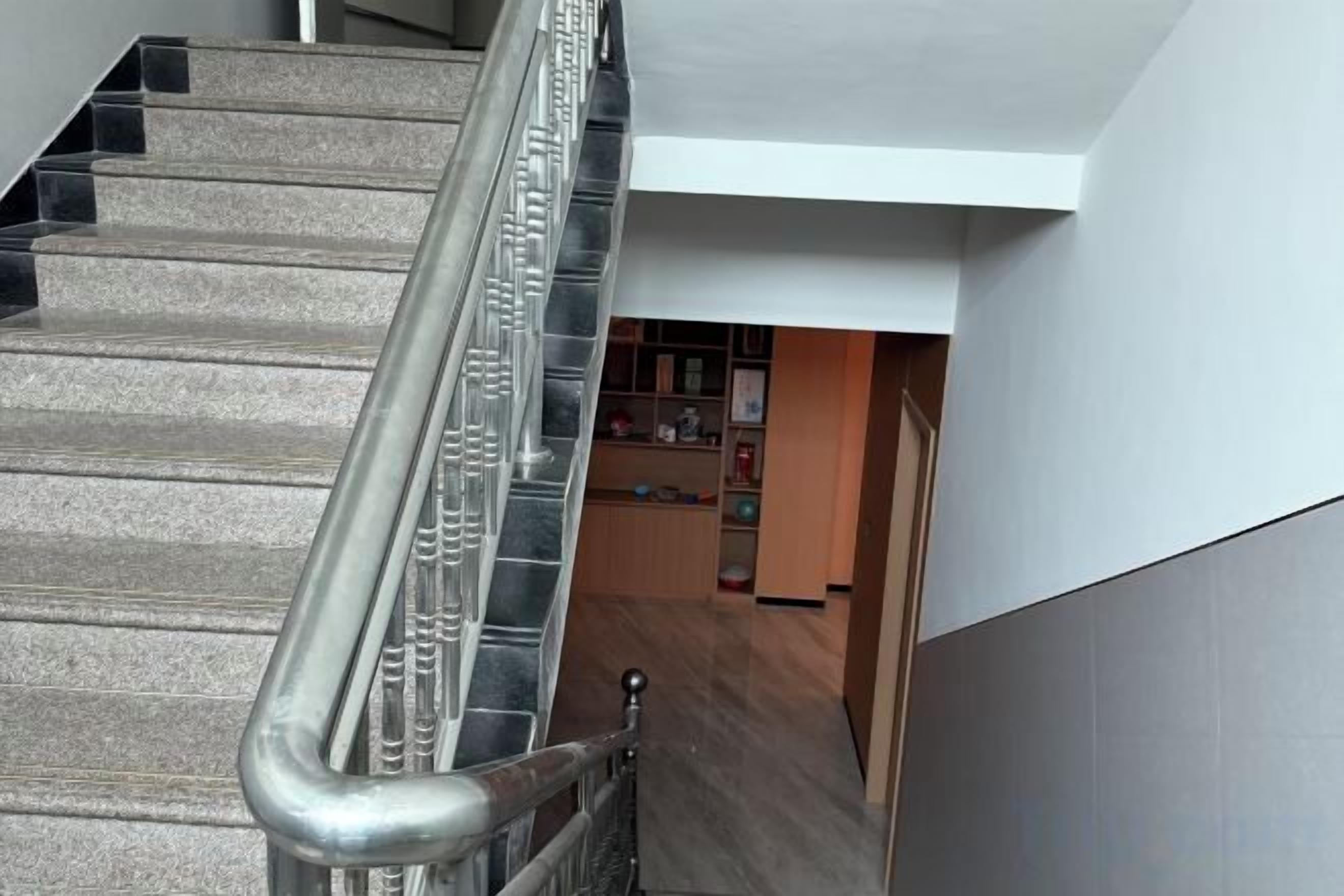 A staircase with metal handrails leading to a room with a wooden floor and a white wall.