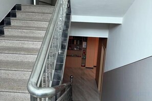 A staircase with metal handrails leading to a room with a wooden floor and a white wall. - Shitai New Century Hotel (Shitai)