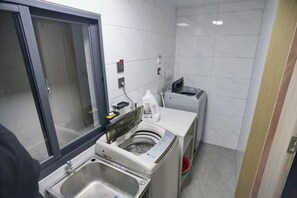 A small, clean kitchen with a sink, a washing machine, and a trash bin. - Shitai New Century Hotel (Shitai)