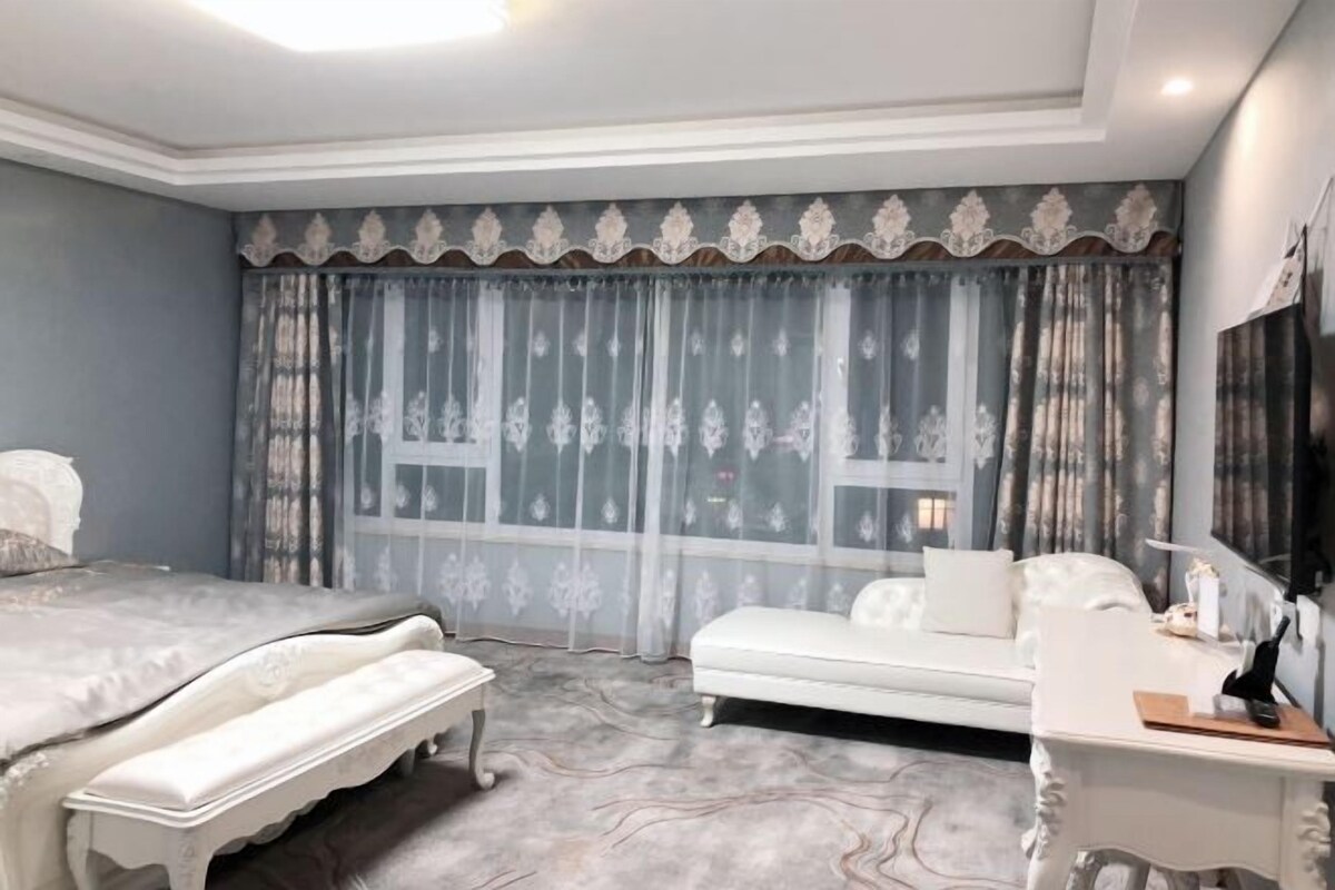 A bedroom with a bed, a bench, a sofa, a desk, and a TV.