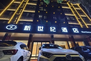 A hotel entrance with illuminated signage and parked cars.
