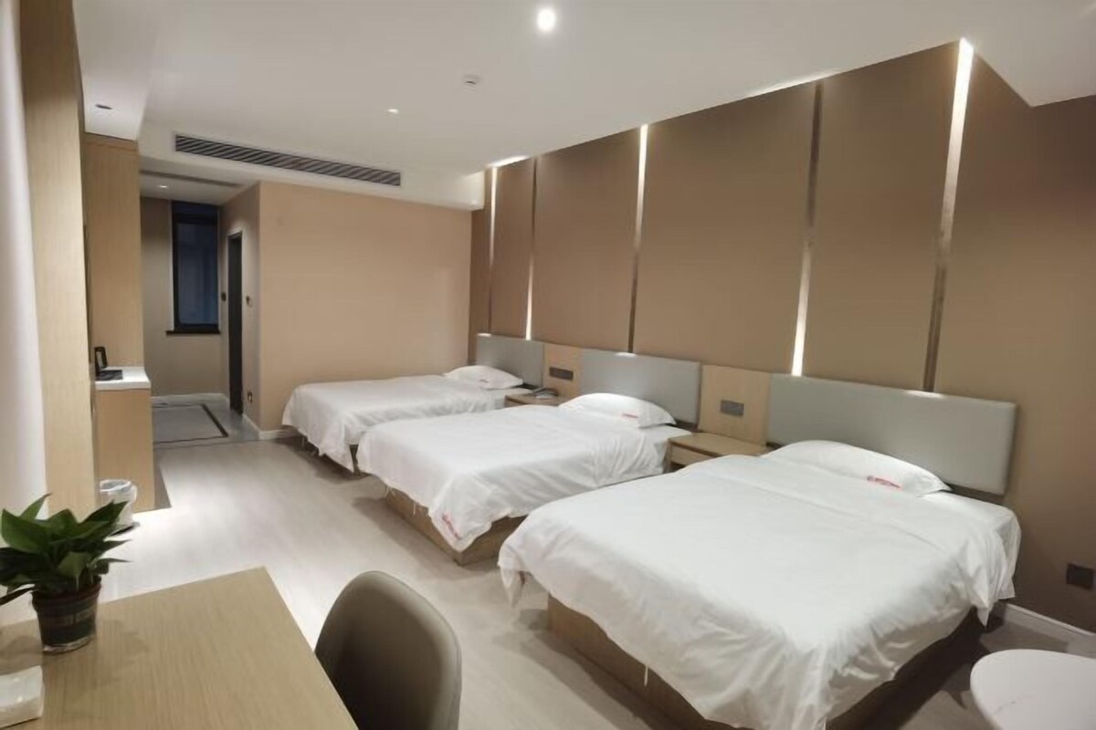 A hotel room with two beds, a desk, a chair, and a potted plant.