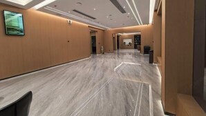Un couloir d’hôtel moderne avec un sol en marbre, des murs lambrissés, un éclairage encastré et un téléviseur fixé au mur.