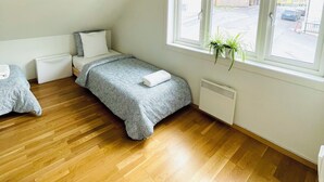 A bedroom with two beds, a radiator, a window with a view of the street, and a ceiling fan. - Central Economic Stavanger (Stavanger)